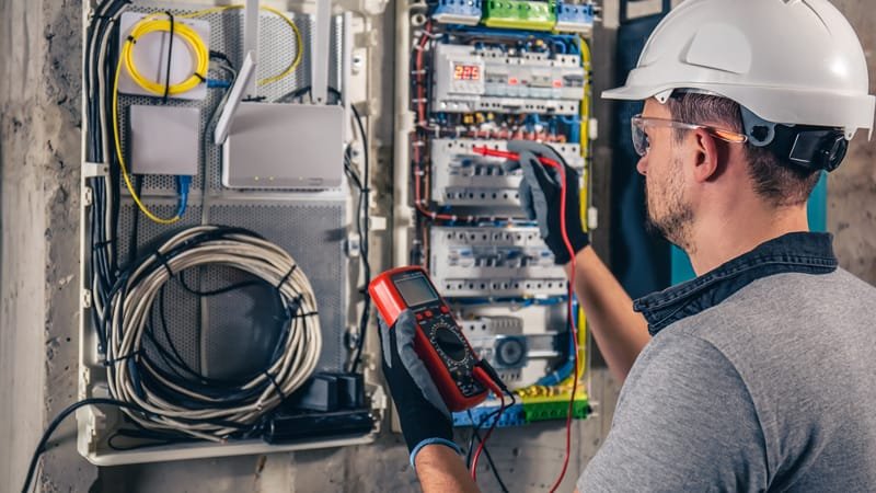 Électricien contrôlant un tableau de distribution au multimètre
